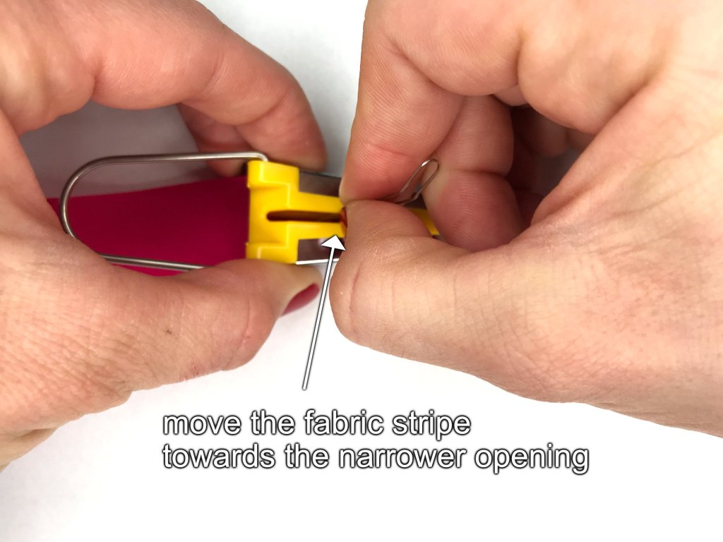 Inserting a stripe of fabric into a bias tape maker using a pin.