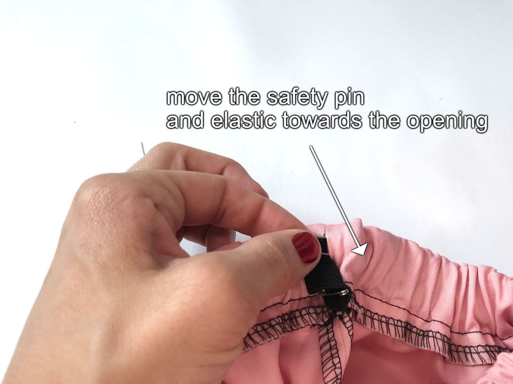 Moving a safety pin with the attached elastic through the waistband casing.