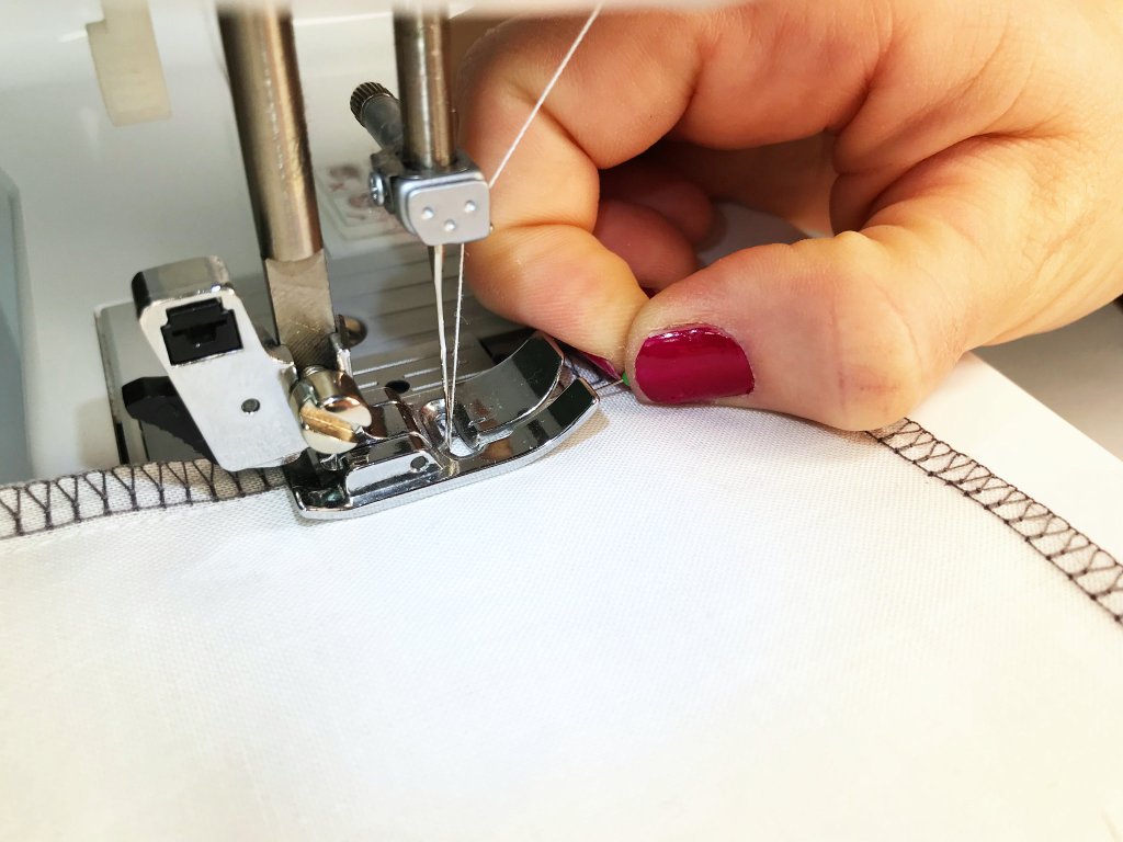 Pulling a pin out from fabric just before a presser foot of a sewing machine.