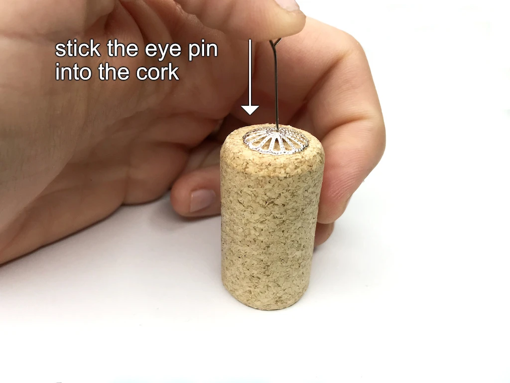 Sticking an eye pin into a bottle cork through a bead cap.
