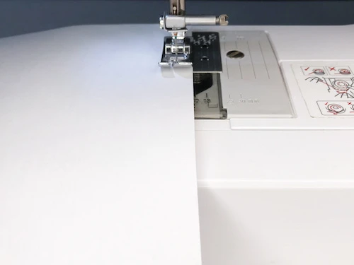 Sewing straight stitches along a paper edge.
