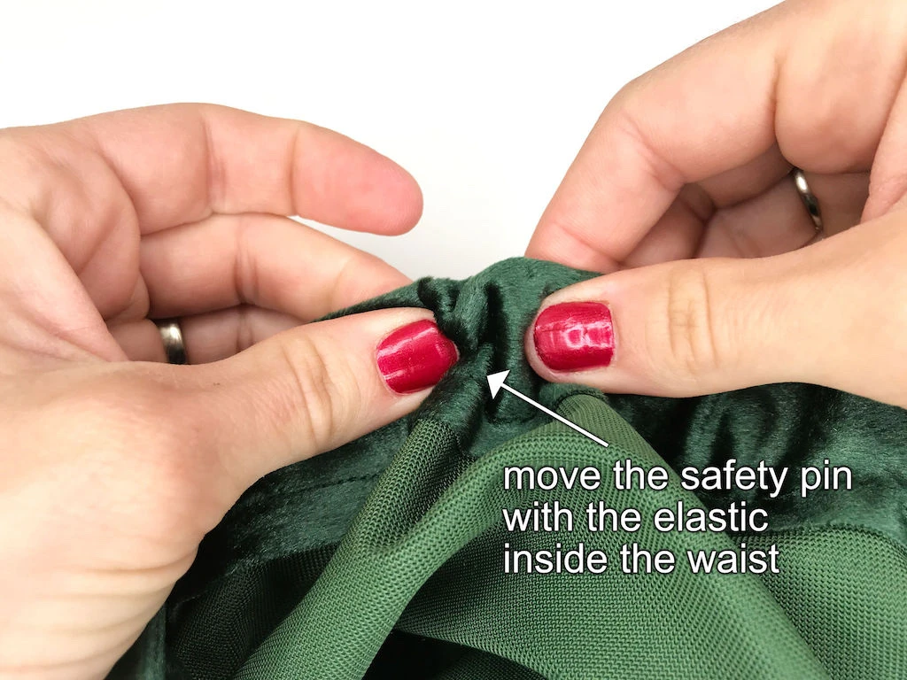 Moving a safety pin with attached elastic band through a gathered skirt waistband casing.